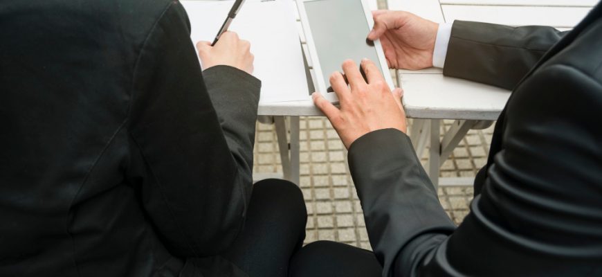 close up businessman businesswoman holding smart phone writing paper outdoors